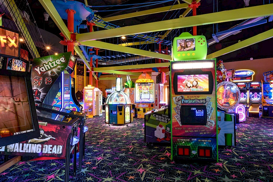 An arcade full of colorful vintage-style games and neon-lit machines, zombies and sci-fi themes, starry carpet, and playful arcade chaos.