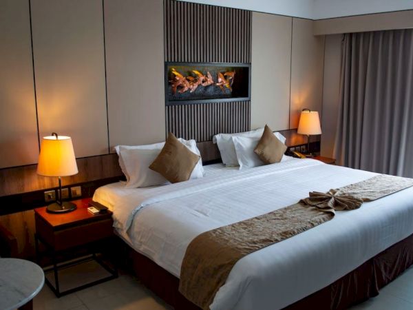 A modern hotel room with a large bed, two bedside tables, lamps, decorative pillows, wall art, and curtains near a window completes the setup.