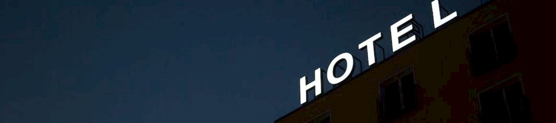 The image shows the top part of a building with a sign that reads "HOTEL" at night, with one letter not fully illuminated.