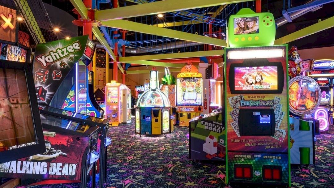 A colorful arcade with various game machines and vibrant lighting on a patterned carpet floor.