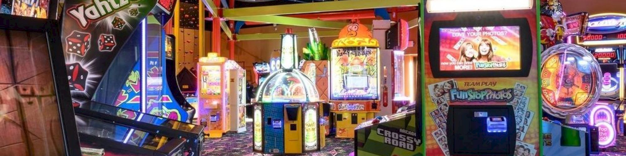 A colorful arcade with various game machines and vibrant lighting on a patterned carpet floor.