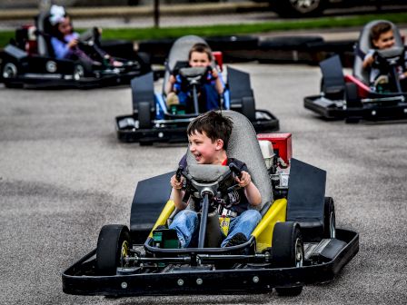 Children are enjoying themselves while driving go-karts on a track, with one child smiling and focusing ahead.