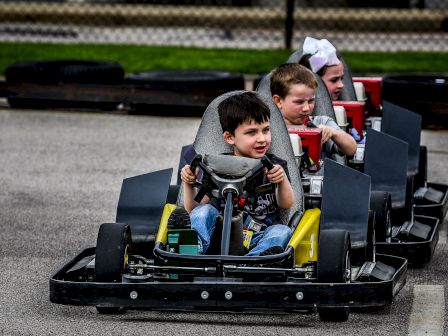 Children are driving go-karts on a track, with one boy in the lead, followed by two other children.