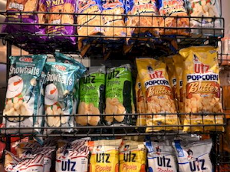 A display rack filled with various Utz snack products, including popcorn, Snowballs, party mix, and ridged cut chips in different flavors and colors.