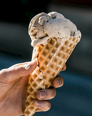 A hand is holding a waffle cone filled with two scoops of ice cream.