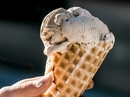 A hand is holding a waffle cone filled with two scoops of ice cream.