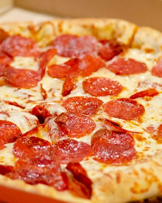 A freshly-baked pepperoni pizza in an open box, featuring a golden-brown crust and melted cheese topped with generous pepperoni slices.