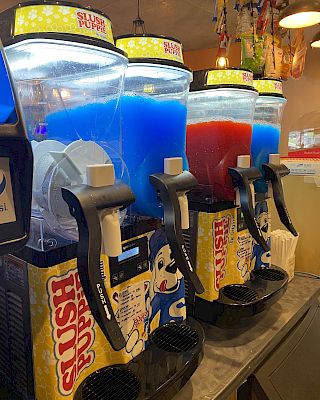 The image shows a row of slushie machines with blue and red slush flavors, labeled 