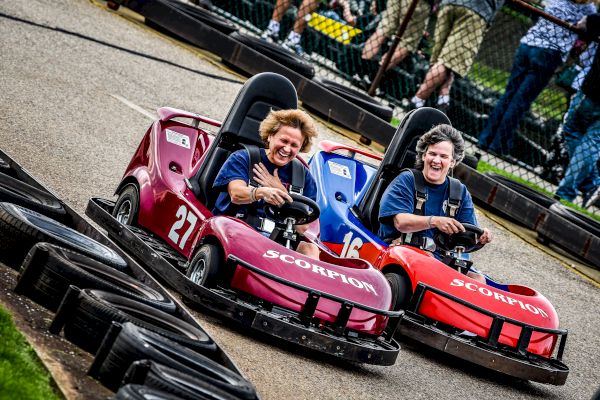 Two people are racing in colorful go-karts on a track, smiling and having fun.