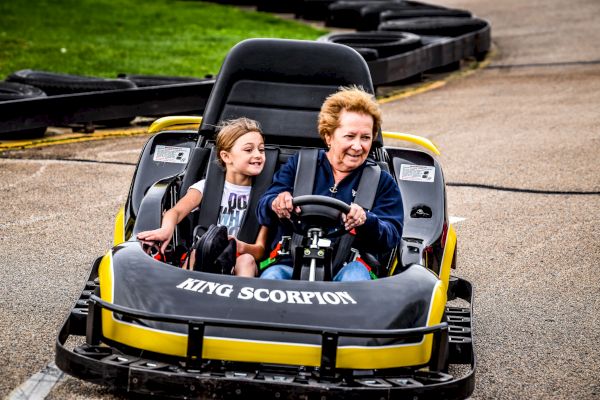 Two people enjoy a ride in a yellow go-kart labeled 