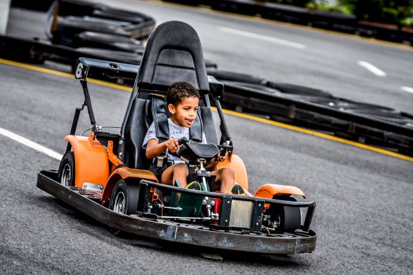 A young boy is driving a go-kart on an outdoor track, looking excited and thrilled as he navigates the course.