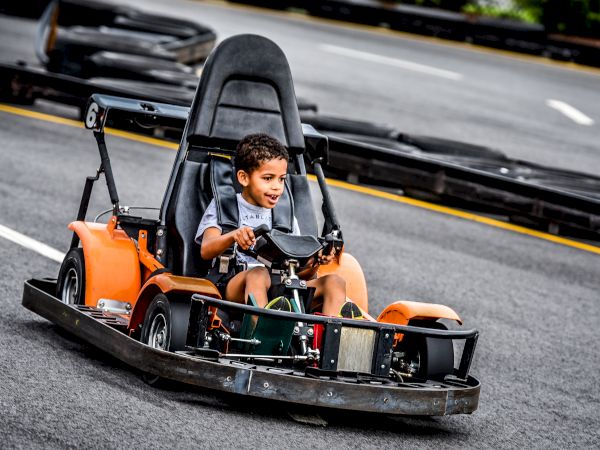 A young boy is driving a go-kart on an outdoor track, looking excited and thrilled as he navigates the course.