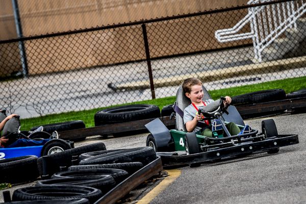 Two children are driving go-karts on a track surrounded by tires as barriers.