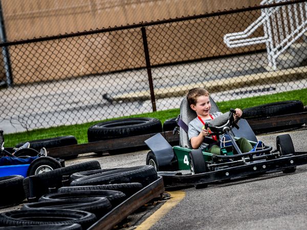 Two children are driving go-karts on a track surrounded by tires as barriers.