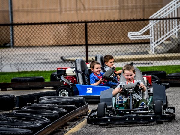 Three children are driving go-karts on an outdoor track, all appearing focused and enjoying the activity.