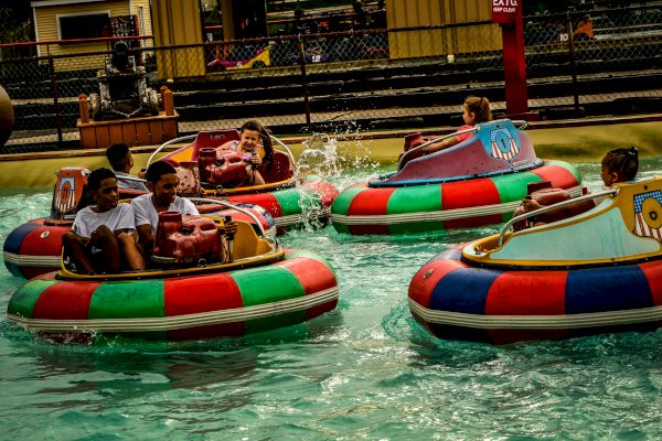 People are enjoying a ride in colorful bumper boats on the water, splashing and laughing, at what appears to be an amusement park.