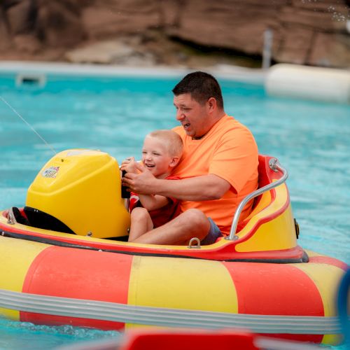 A man and child are enjoying a ride in a colorful bumper boat in a pool, smiling and having fun.