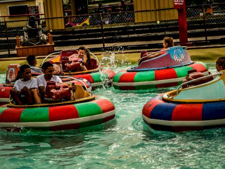 People are riding colorful bumper boats in a pool, splashing water and having fun at an amusement park.