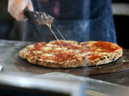 A person is cutting a freshly baked pizza with a pizza cutter, and mozzarella cheese is stretching from the slices.