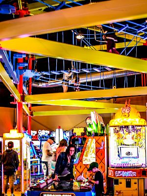 This image shows a vibrant indoor amusement park with arcade games, colorful structures, and people enjoying various activities.