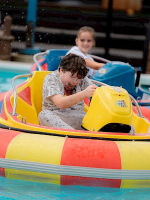 Children are enjoying a ride in colorful bumper boats at a pool, having fun in a waterpark-like setting.