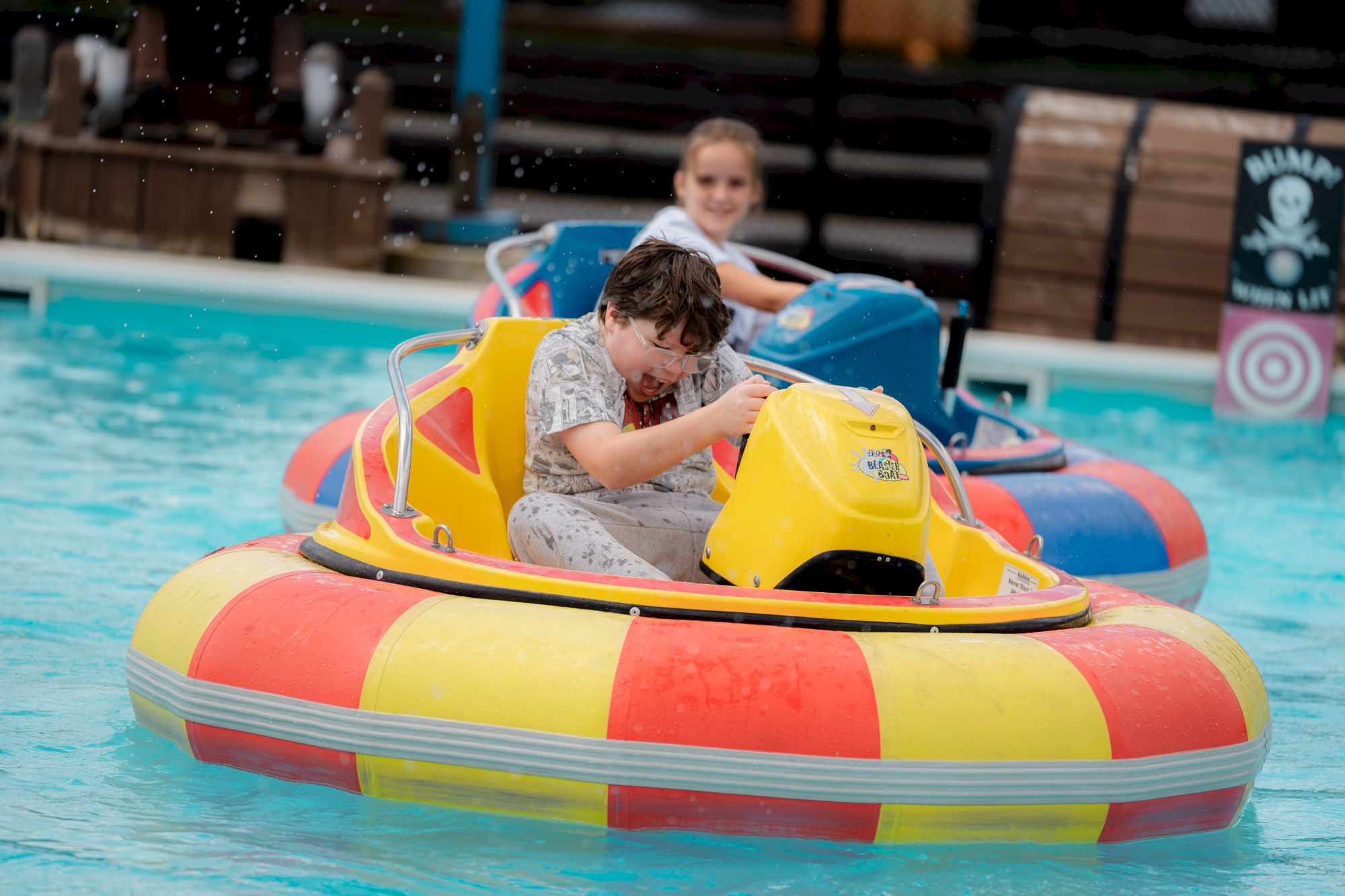 Children are playing on colorful bumper boats in a pool, having fun with water splashing around them.