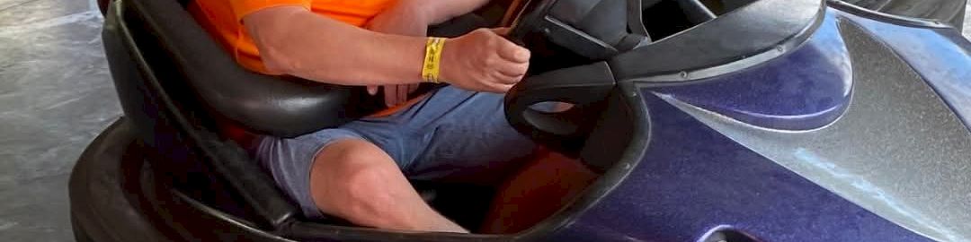 A man and a child ride a bumper car together with another person in the background, all in a fun amusement setting.