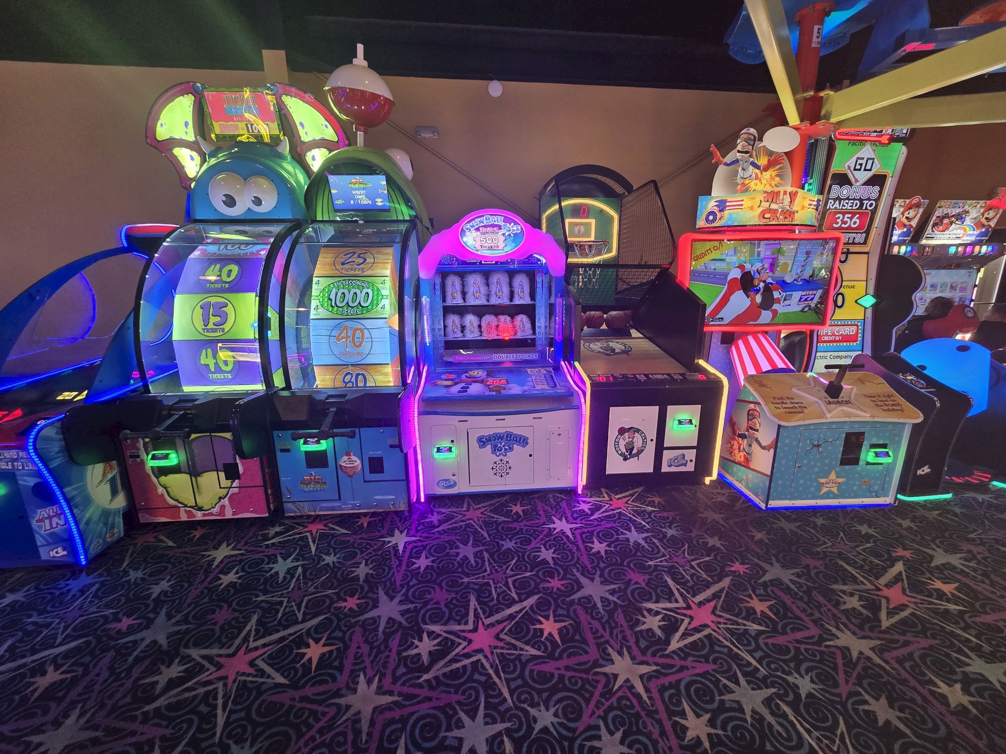 A row of colorful arcade game machines and slot-style cabinets in a dimly lit arcade room, with bright neon lights and star-patterned carpet, ending这里.