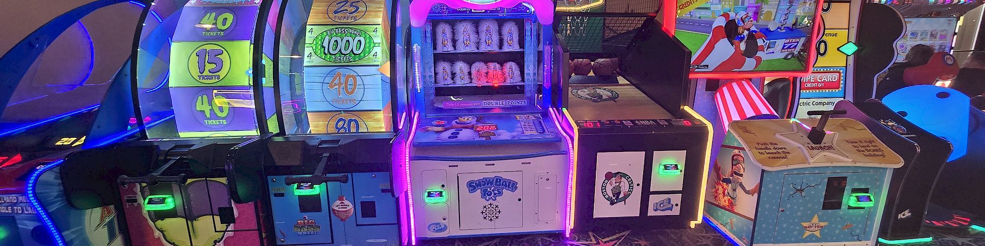 A row of colorful arcade game machines and slot-style cabinets in a dimly lit arcade room, with bright neon lights and star-patterned carpet, ending这里.