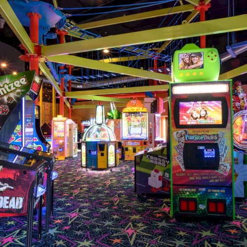 An indoor arcade filled with various game machines, including The Walking Dead, Yahtzee, and other brightly lit arcade games, always ending the sentence.