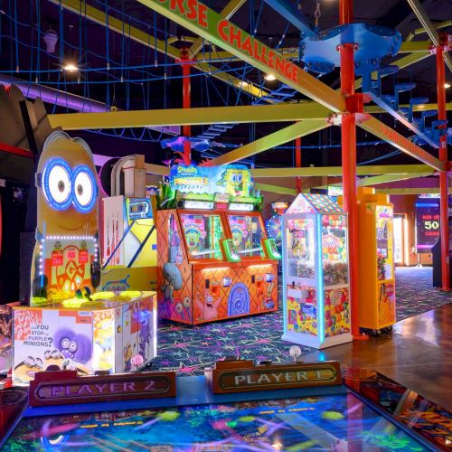 The image shows a colorful indoor arcade with various games, claw machines, and a high ropes course above.