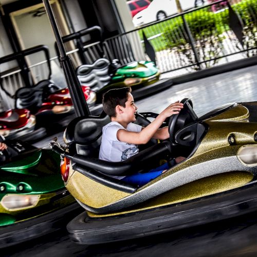 A boy and a woman are riding bumper cars in an amusement park. The boy is in a gold car while the woman is in a green one, enjoying the ride.