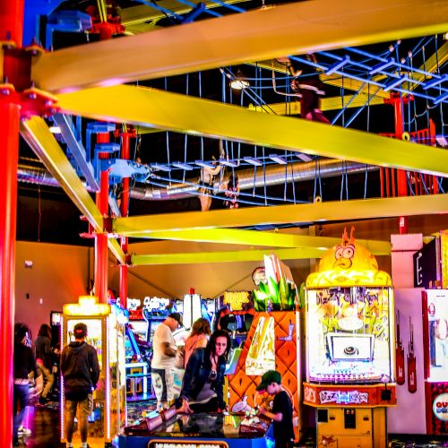 This image shows a lively arcade with vibrant games, a jungle gym above, and people enjoying the various entertainment options.