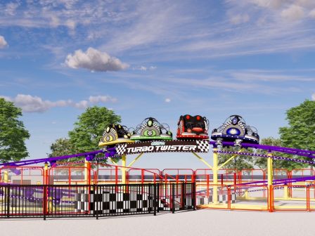 A colorful amusement-park rollercoaster, Turbo Twister, with cartoon cars on a bright track beneath leafy trees under a blue sky.