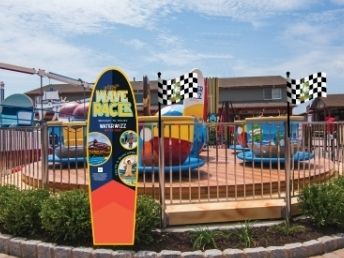 A colorful amusement playground with slides and a &ldquo;Track Racer&rdquo; sign under a bright blue sky.