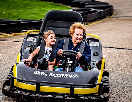 A woman and a child ride a small “Tiny Scorpion” go-kart together on a paved track.