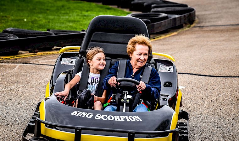 A woman and a child ride a small “Tiny Scorpion” go-kart together on a paved track.