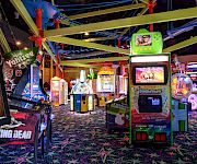 A neon arcade game area with a big photo kiosk booth, trampolines, and colorful lighted attractions.