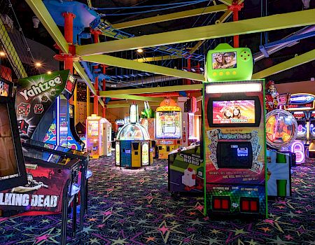 A neon arcade game area with a big photo kiosk booth, trampolines, and colorful lighted attractions.