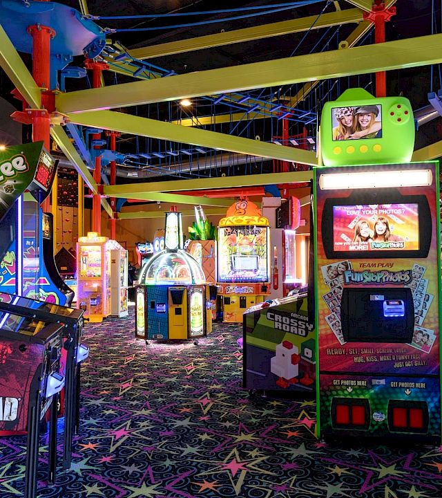 A neon arcade game area with a big photo kiosk booth, trampolines, and colorful lighted attractions.