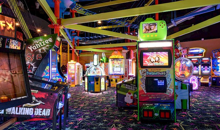 A neon arcade game area with a big photo kiosk booth, trampolines, and colorful lighted attractions.