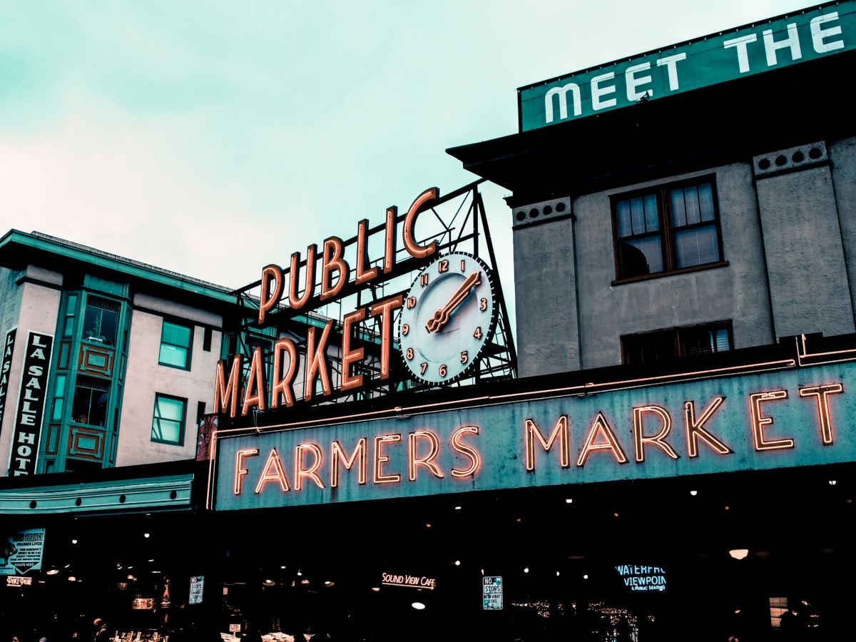 The image shows a well-known marketplace with neon signs that read "Public Market" and "Farmers Market" on a building.